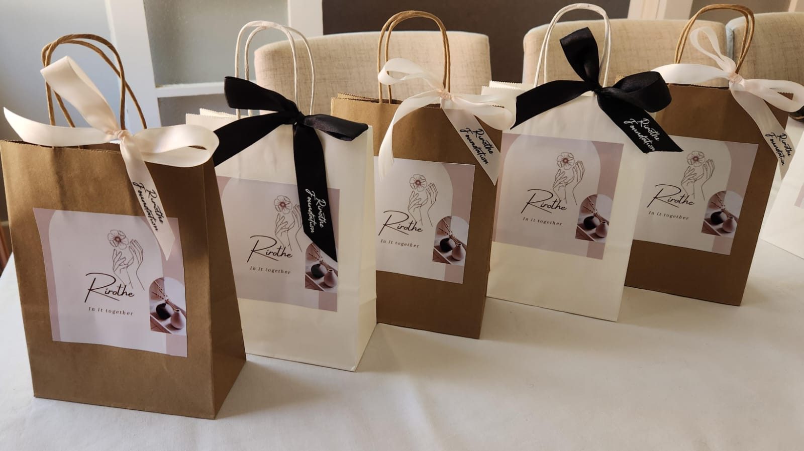 Rirothe Foundation gift bags tied with black ribbon, each carrying the flower-and-hands label.