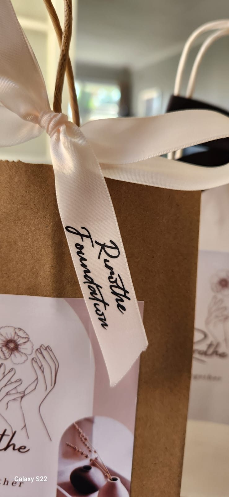 A cream satin ribbon printed with the Rirothe Foundation script, tied to a kraft paper bag.